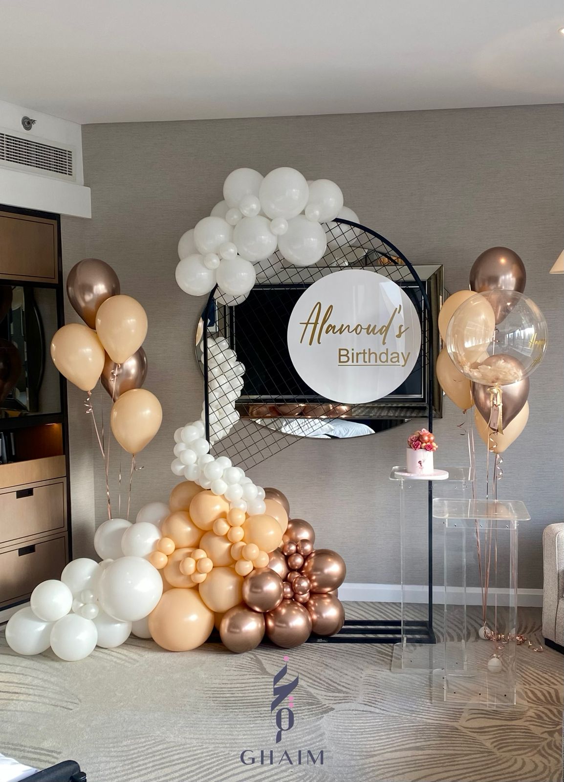 Elegant neutral-toned birthday décor with a circular wire backdrop and custom sign, ivory and beige balloon garland, helium balloon bouquets, and clear acrylic stands