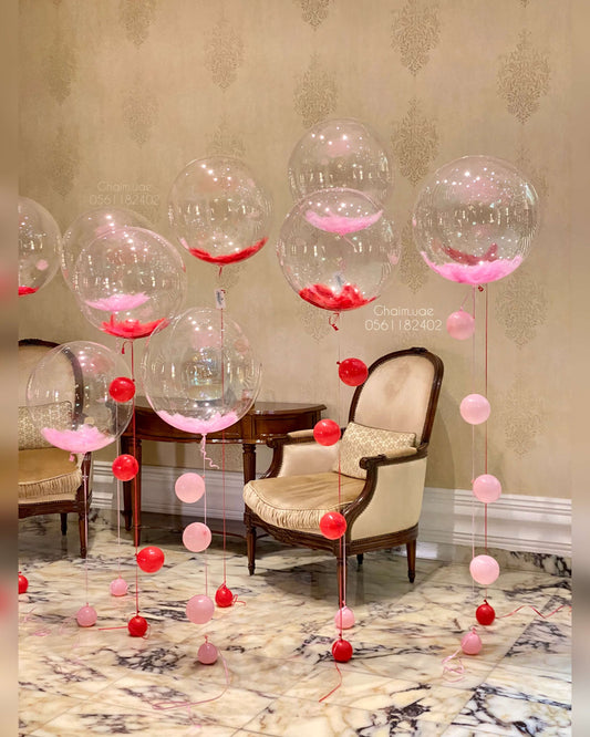 Clear helium bubble balloons with pink feathers and red and pink balloon tails