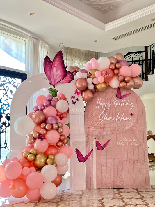 Pink and gold butterfly-themed birthday balloon backdrop with custom text sign