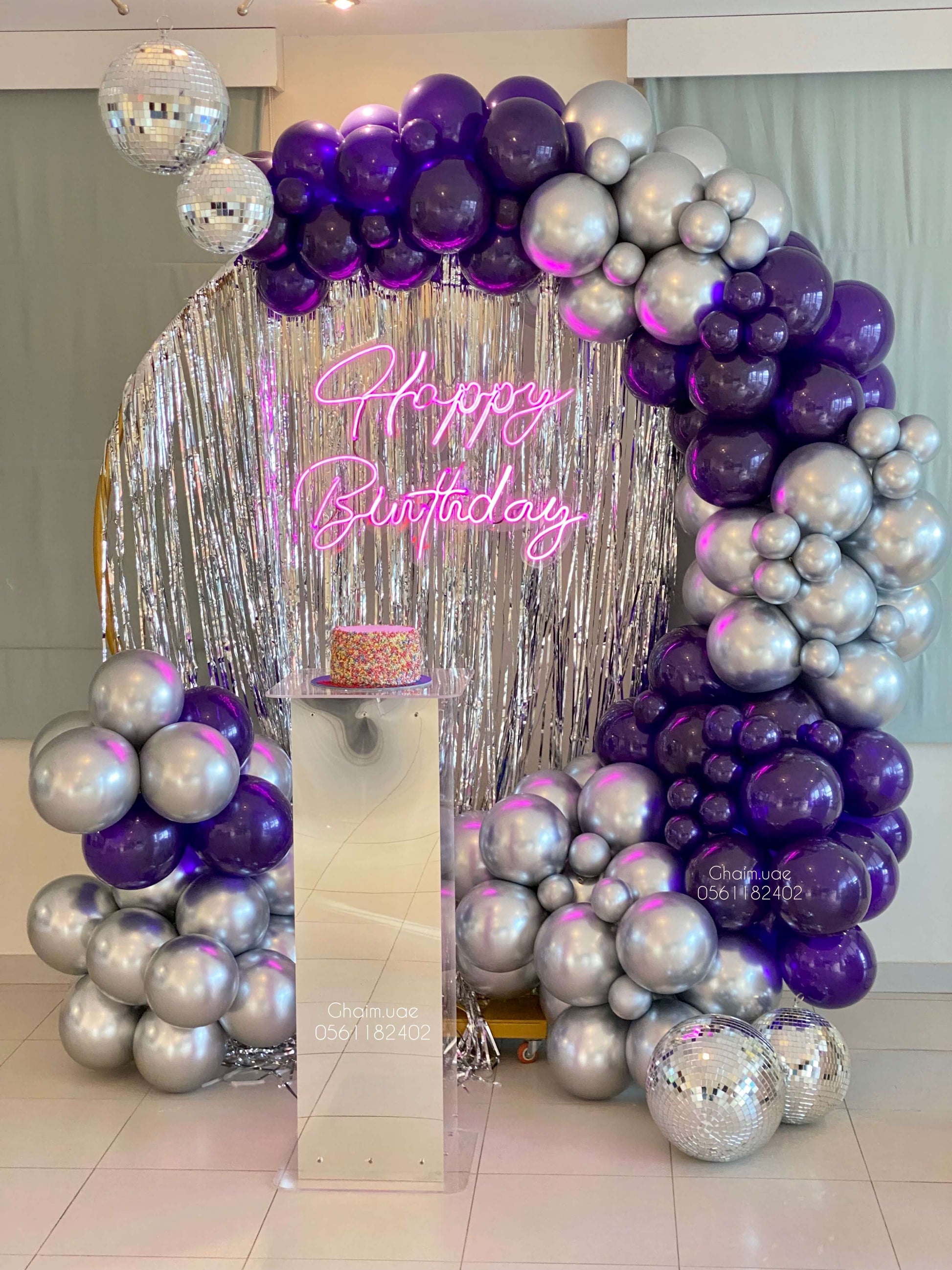 Purple and silver balloon backdrop with fringe curtain, disco balls, and neon custom text sign