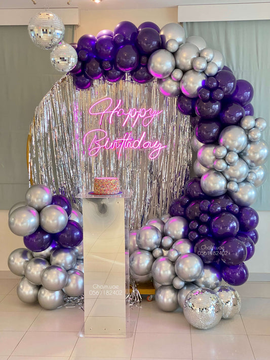 Purple and silver balloon backdrop with fringe curtain, disco balls, and neon custom text sign