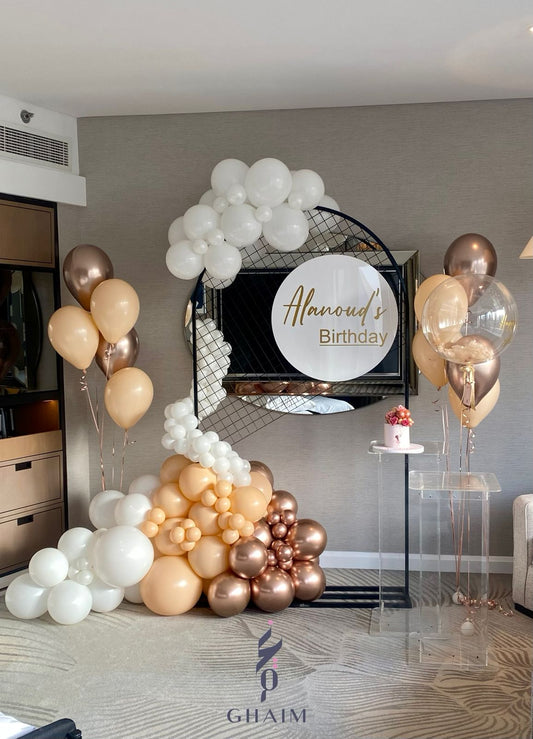 Elegant neutral-toned birthday décor with a circular wire backdrop and custom sign, ivory and beige balloon garland, helium balloon bouquets, and clear acrylic stands